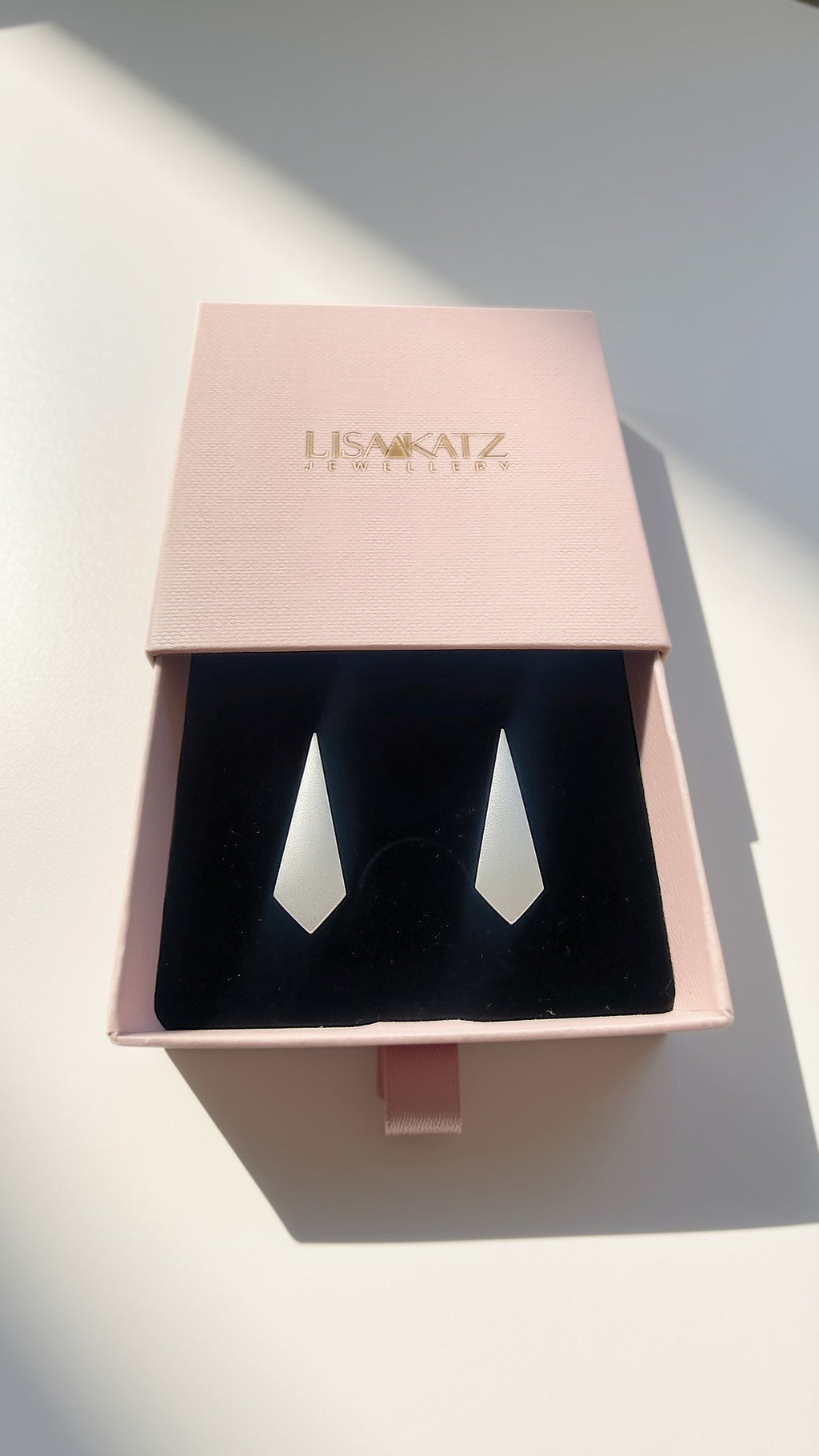 A pair of silver geometric drop earrings displayed in a pink presentation box with a black velvet insert. The brand name 'LISA KATZ JEWELLERY' is printed in gold on the pink lid.