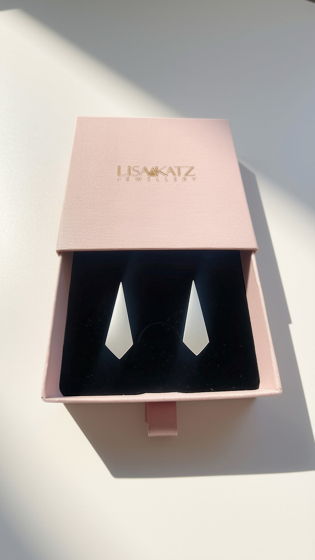 A pair of silver geometric drop earrings displayed in a pink presentation box with a black velvet insert. The brand name 'LISA KATZ JEWELLERY' is printed in gold on the pink lid.