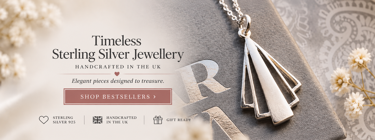 Sterling silver geometric pendant necklace on a textured gray book, with decorative dried flowers and text overlays reading 'Timeless Sterling Silver Jewellery' and 'Handcrafted in the UK'.